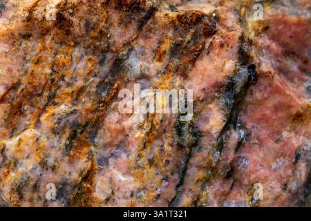 Primo piano di una pietra di colore rosa con macchie gialle e nere sparse, che mostrano motivi e texture naturali unici Foto Stock