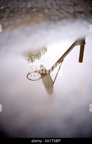 Canestro da basket che si riflette nella pozzanghera dopo la doccia a pioggia Foto Stock