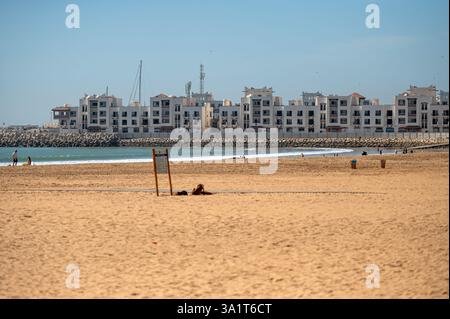 Agadir, Marocco - 21 febbraio 2025: Le persone si rilassano sulla spiaggia di sabbia mentre le residenze costiere si affacciano sull'oceano di Agadir. Foto Stock