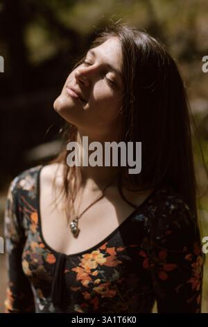 Una donna a occhi chiusi gode di una luce solare calda in natura Foto Stock