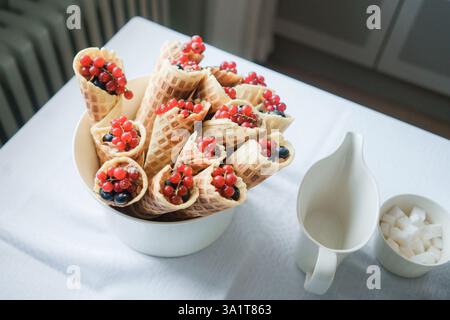 Cialde in coni con frutti di bosco in una ciotola bianca sul tavolo. Bar di dolci per matrimoni. Foto Stock