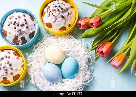Torte di Pasqua, uova dipinte nel nido e tulipani su sfondo blu. Layout piatto. Vista dall'alto. Foto di alta qualità Foto Stock