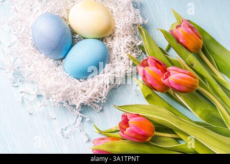 Uova di Pasqua in un nido bianco e tulipani rosa su sfondo azzurro. Vista dall'alto. Layout piatto. Foto di alta qualità Foto Stock