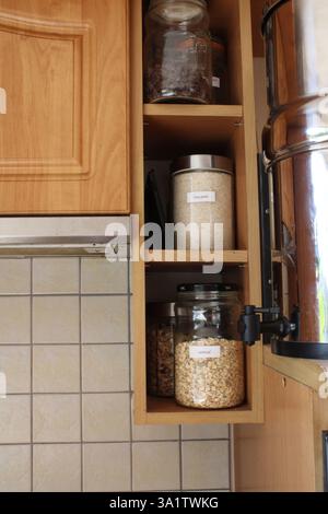 Un ripiano in legno con vasetti di vetro ripieni di riso, farinata d'avena, pezzi di cioccolato, basmati, ingredienti alimentari, mobili in legno, interni, cucina casalinga Foto Stock