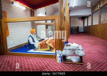 Un prete sikh in un turbante giallo legge dal libro sacro di Guru Granth Sahib in un tempio vicino al tempio vacante di Richmond Hill, Queens, New York City. Foto Stock