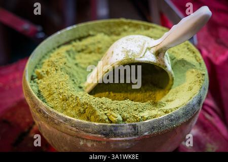Primo piano di un recipiente in metallo contenente polvere verde brillante di matcha con un misurino posizionato all'interno Foto Stock