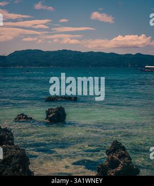 Le limpide acque turchesi si infrangono dolcemente contro rocce scure sulla spiaggia bianca di boracay, filippine. Foto Stock