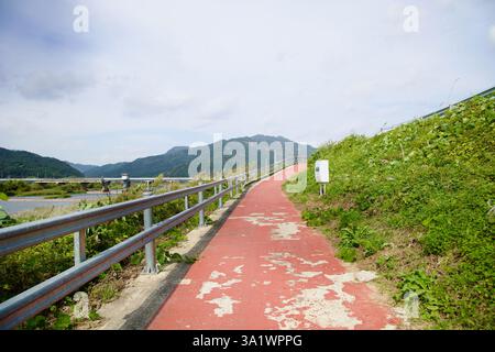 Namwon City, Corea del Sud - 3 ottobre 2021: Una pista ciclabile rossa intemprata con curve di vernice che si staccano in salita lungo una ringhiera di metallo che si affaccia sul Foto Stock