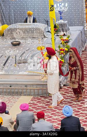 Durante un matrimonio Sikh, la sposa e lo sposo camminano intorno all'altare dove un sacerdote legge il Guru Granth Sahib. A New York. Foto Stock