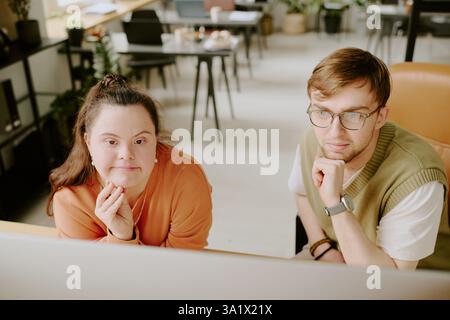 Ripresa ad angolo elevato di due specialisti IT caucasici appoggiati alla testa durante la lettura dei codici sullo schermo del computer Foto Stock