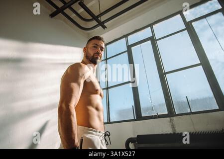 Un uomo forte posa con sicurezza in un ambiente da palestra illuminato e vibrante Foto Stock