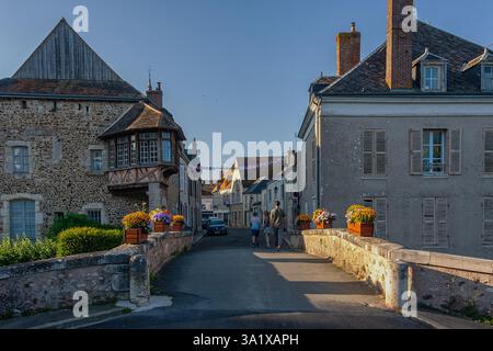I turisti attraversano un ponte medievale in pietra, ammirando l'architettura storica e tradizionale del villaggio di Bonneval. Bonneval, Francia Foto Stock