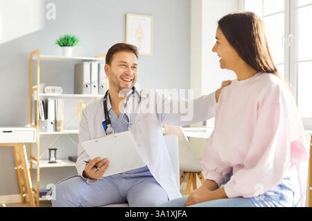 Allegro maschio medico supporto giovane paziente sorridente donna seduta in clinica medica Foto Stock
