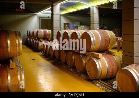 Una lunga fila di botti di vino si estende attraverso il deposito sotterraneo della cantina. Foto Stock