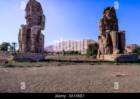 I Colossi di Memnone sono due enormi statue in pietra del faraone Amenofi III, che si trovano di fronte al Tempio Mortuario in rovina di Amenofi III Foto Stock