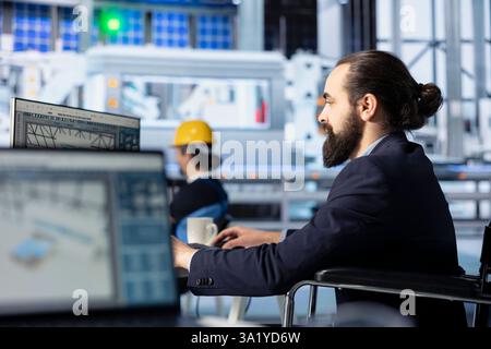 Ingegnere di fabbrica fotovoltaico che guarda lo schermo del PC, regolando i parametri del sistema. Tecnico che ottimizza la fornitura di energia nell'impianto di produzione di pannelli solari utilizzando un monitor computerizzato Foto Stock