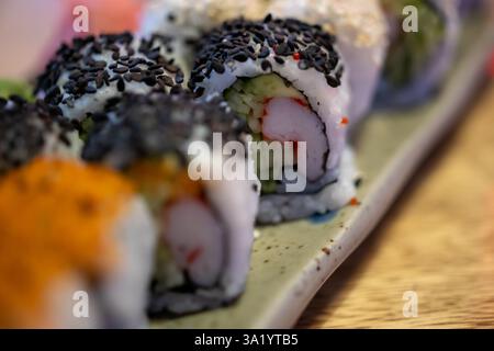 piatto di sushi con vari condimenti e ripieni, disposti su un tavolo di legno. Il sushi è decorato con semi di sesamo nero, semi di sesamo bianco Foto Stock
