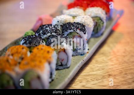 piatto di sushi con vari condimenti e ripieni, disposti su un tavolo di legno. Il sushi è decorato con semi di sesamo nero, semi di sesamo bianco Foto Stock