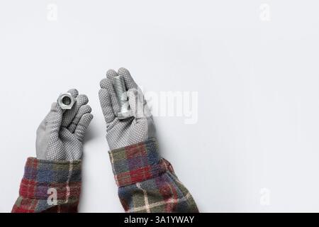 Le mani del meccanico tengono il bullone e il dado su sfondo grigio Foto Stock
