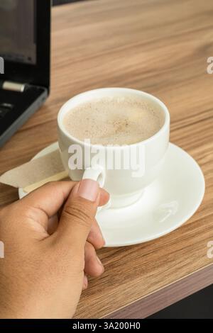 Una mano impugna l'impugnatura di una tazza piena di deliziosa cioccolata calda fumante, pronta ad assaporare il calore rilassante. Foto Stock