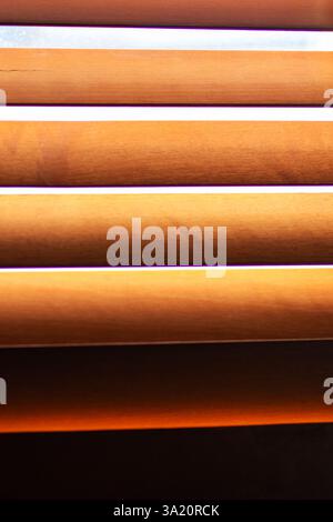 Questa immagine mostra una vista ravvicinata di una tenda in legno splendidamente realizzata, con una luce solare brillante che scorre attraverso le sue spranghe, creando un'atmosfera calda Foto Stock