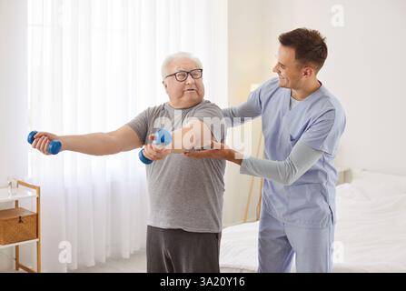 Uomo anziano che fa esercizi con manubri con l'aiuto di fisioterapista professionista Foto Stock