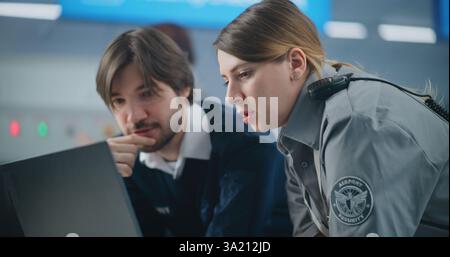Controllo di sicurezza aeroportuale: Primo piano di due diversi agenti di sicurezza che utilizzano computer portatile e parlano. Transport Security Administration for Travel Safety (Amministrazione per la sicurezza dei trasporti). In background, il personale aeroportuale che lavora Foto Stock