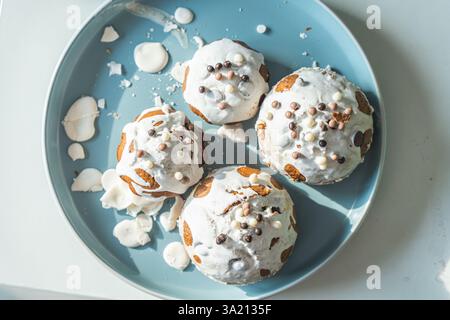 Muffin o cupcake ricoperti di glassa bianca e palline di cioccolato su un piatto azzurro su sfondo bianco. Vista dall'alto. Foto di alta qualità Foto Stock