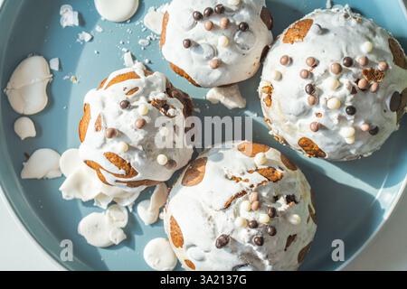 Muffin o cupcake ricoperti di glassa bianca e palline di cioccolato su un piatto azzurro su sfondo bianco. Vista dall'alto. Foto di alta qualità Foto Stock