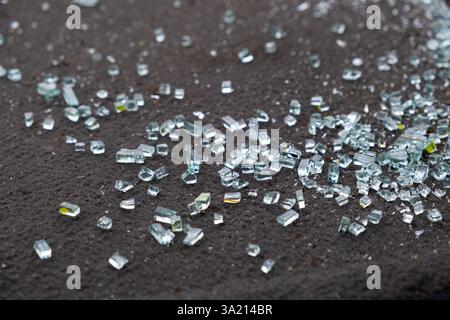Una panoramica dettagliata di piccoli frammenti di vetro rotto disseminati su una superficie scura e ruvida, catturando efficacemente le belle qualità riflettenti e gli aspetti luccicanti dei pezzi di vetro Foto Stock