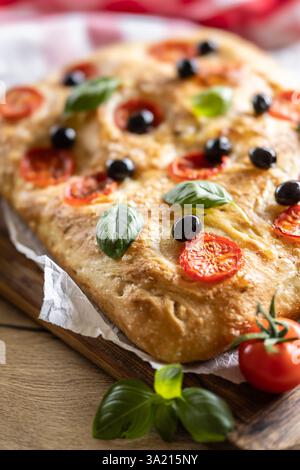 Focaccia - Pane Italiano con pomodori basilico foglie di olive e olio d'oliva sul tagliere. Foto Stock