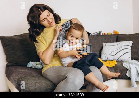 Madre che cambia il suo bambino, mentre il bambino ride, tenendo in mano un'auto giocattolo. Foto di alta qualità Foto Stock