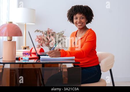 Donna afro-americana sorridente che lavora con un laptop a casa con un notebook Foto Stock
