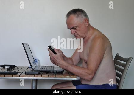 Uomo d'affari, libero professionista, più di 60 anni in vacanza lavorando con computer portatile e telefono cellulare, Pattaya, Chonburi, Thailandia, Asia Foto Stock