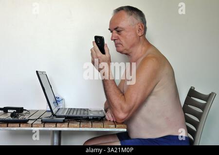 Uomo d'affari, libero professionista, più di 60 anni in vacanza lavorando con computer portatile e telefono cellulare, Pattaya, Chonburi, Thailandia, Asia Foto Stock