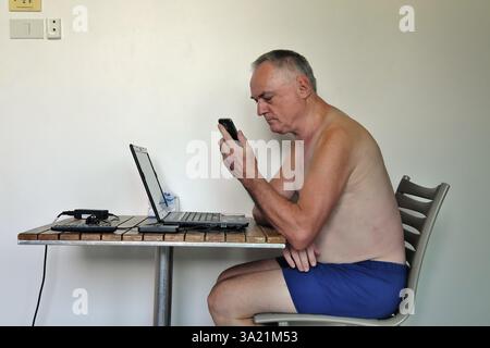 Uomo d'affari, libero professionista, più di 60 anni in vacanza lavorando con computer portatile e telefono cellulare, Pattaya, Chonburi, Thailandia, Asia Foto Stock