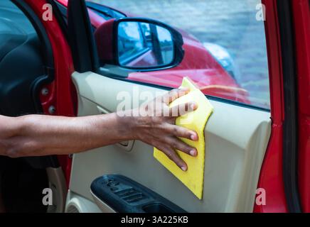 Uomo che pulisce l'auto con dettagli e concetti di pulizia in tessuto in microfibra. La mano di un lavoratore utilizza un panno in microfibra giallo pulito per pulire la vettura dopo essere stata Foto Stock