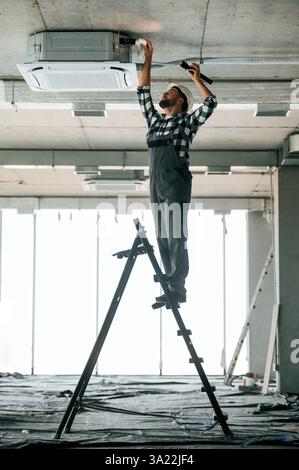 In piedi sulla scala. Il riparatore in uniforme è nell'edificio incompiuto. Foto Stock