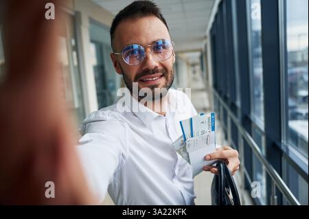 Fare selfie, un'espressione facciale felice. Giovane bell'uomo all'aeroporto. Foto Stock