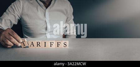 Mano che posa blocchi di legno con la parola tariffe, concetto di tariffe commerciali, economia, politica e governo su sfondo grigio Foto Stock