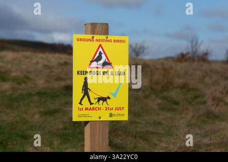 Un cartello giallo che chiede che i cani siano tenuti in piombo durante la stagione degli uccelli nidificanti a Baildon Moor nello Yorkshire. Foto Stock