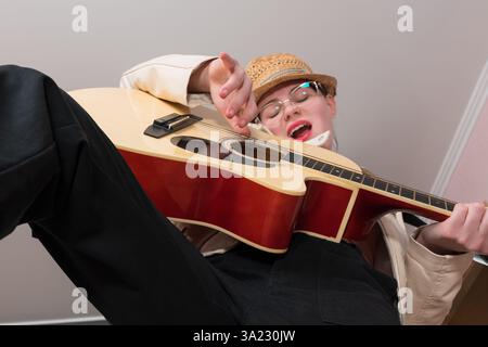 Chitarrista e cantautrice femminile espressiva che suona la chitarra acustica e canta la canzone con gli occhi chiusi. Vista ad angolo basso della chitarrista donna, selectiv Foto Stock