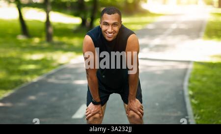 Sorridente jogger nero riposante dopo maratona correre in un parco soleggiato Foto Stock