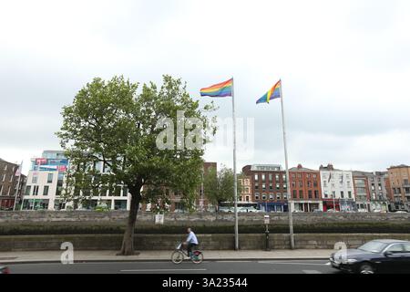 Dublino, Irlanda - 25 giugno 2014 - le bandiere arcobaleno lgbt volano su palafitte accanto ad un albero lungo le banchine del fiume Liffey mentre un ciclista passa Foto Stock