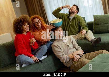 Quattro amici si riuniscono in un accogliente soggiorno, ridendo e godendosi la compagnia degli altri mentre condividono popcorn e bevande mentre guardano un film su una com Foto Stock