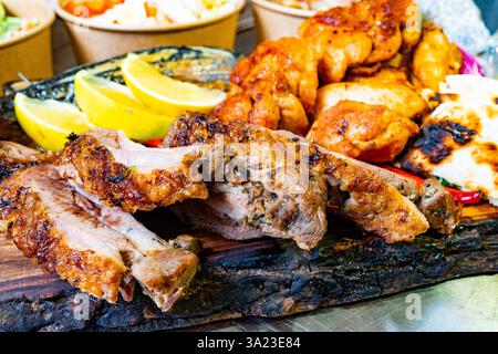 Un'appetitosa selezione di carni alla griglia servite su una tavola di legno presenta succulente costolette, pollo speziato e fette di limone fresche. Lati colorati co Foto Stock