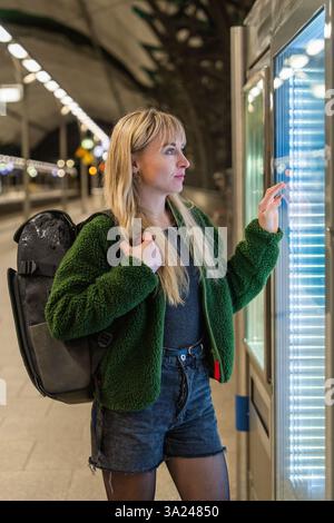 La ragazza con lo zaino sta in piedi sulla piattaforma in attesa del treno di sera. Inizia un viaggio indipendente. In attesa del viaggio Foto Stock