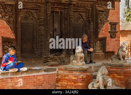 Dunbar Square, Bhaktapur, Nepal - 10 febbraio 2025 - Vecchio e giovane sedevano in un antico tempio buddista in Nepal Foto Stock