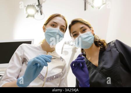 Dal basso dentisti con specchio e dispositivo piegato sopra la paziente durante l'appuntamento in clinica odontoiatrica. Foto Stock