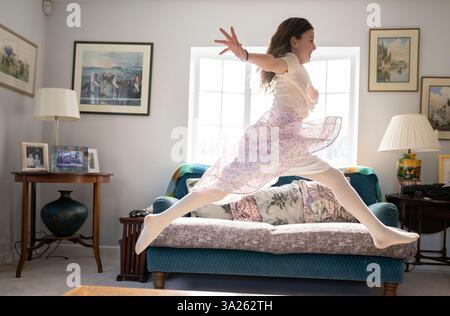 Ragazza che salta gioiosamente attraverso il salotto con le braccia allungate. Foto Stock